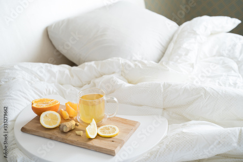 Cup with antipyretic drugs for colds flu.Tea with citrus vitamin C ginger root lemon orange.Wooden tray in patient s bed. Home self-treatment.Medical quarantine antiviral covid-19 coronavirus therapy