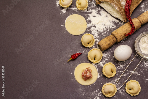 Composition with raw dumplings and ingredients on trendy black stone concrete background. Process of cooking