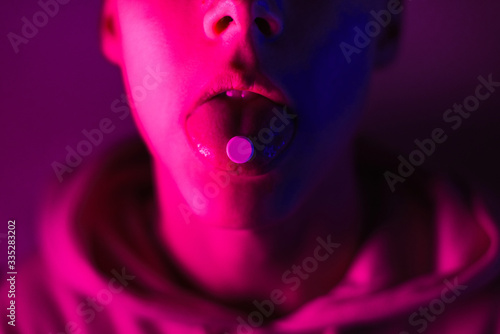 Young teenager in a pink hoodie takes a drug in pills. Tongue guy with lsd wheel