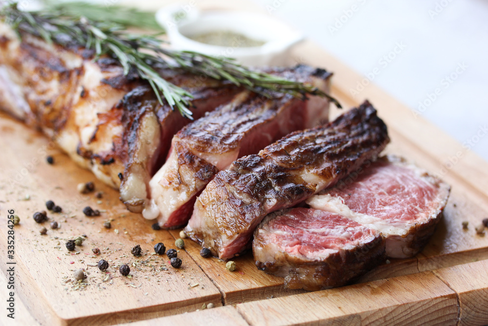Tomahawk beef steak grilled with spices and rosemary on a wooden board on a light background. Slices of meat. Background image, copy space