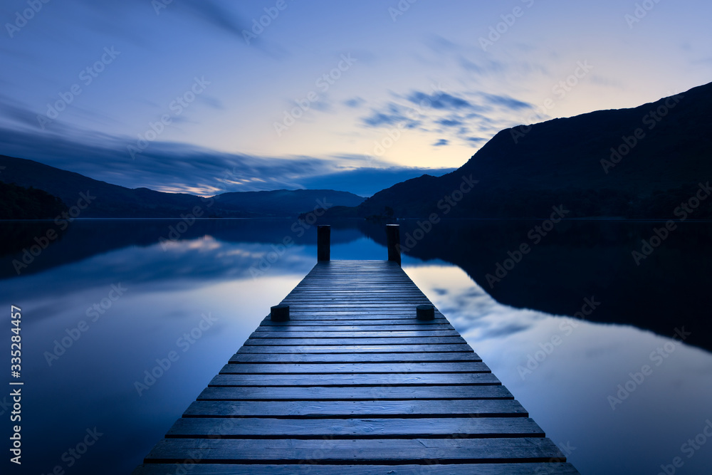 Wooden Jetty/Pier Leading Out To Calm Lake With Reflections At Blue Hour In The Lake District, UK.
