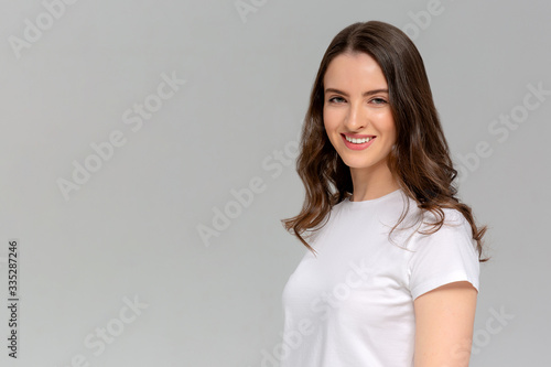 Close up portrait of smiling young woman in white t-shirt looking at camera, isolated on gray background