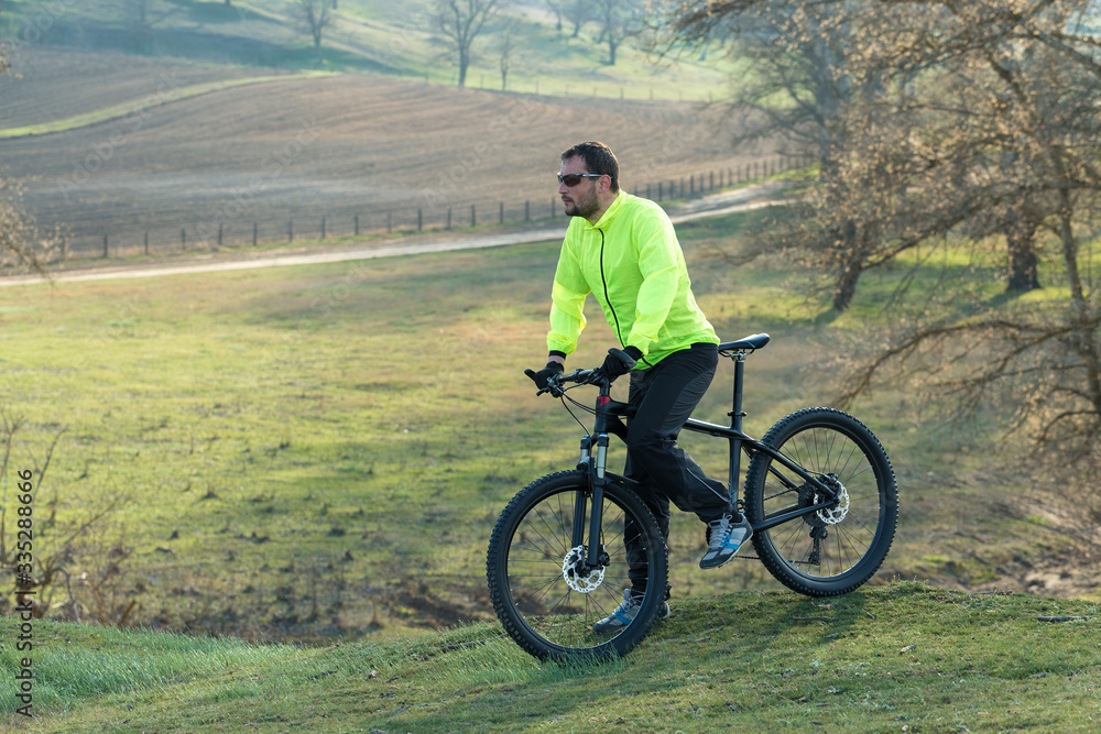 Cyclist in pants and green jacket on a modern carbon hardtail bike with an air suspension fork. The guy on the top of the hill rides a bike. Cyclist in pants and green jacket on a modern carbon hardtail bike with an air suspension fork. The guy on the top of the hill rides a bike.