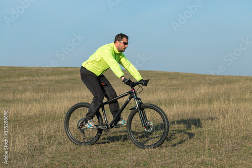 Fototapeta Naklejka Na Ścianę i Meble -  Cyclist in pants and green jacket on a modern carbon hardtail bike with an air suspension fork. The guy on the top of the hill rides a bike.
