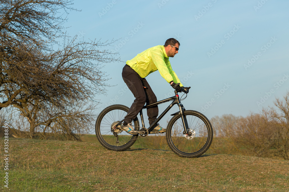 Cyclist in pants and green jacket on a modern carbon hardtail bike with an air suspension fork. The guy on the top of the hill rides a bike. Cyclist in pants and green jacket on a modern carbon hardtail bike with an air suspension fork. The guy on the top of the hill rides a bike.