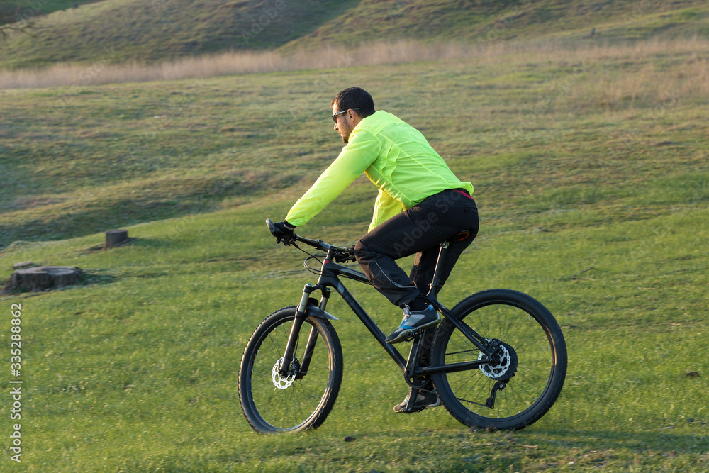 Cyclist in pants and green jacket on a modern carbon hardtail bike with an air suspension fork. The guy on the top of the hill rides a bike. Cyclist in pants and green jacket on a modern carbon hardtail bike with an air suspension fork. The guy on the top of the hill rides a bike.