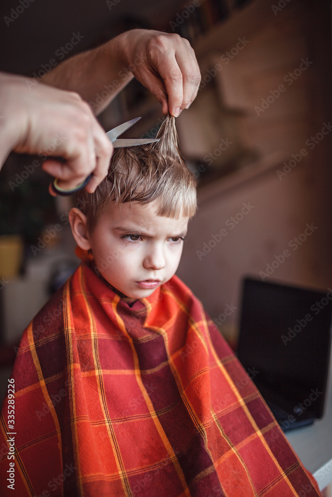 Fototapeta premium Middle aged father cutting hair to his little son by himself at home, life during lockdown