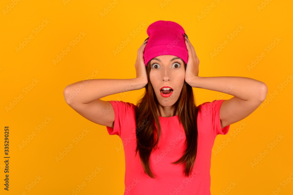 surprised woman in pink hat and t-shirt holding her head on a yellow background portrait surprised woman in pink hat and t-shirt holding her head on a yellow background portrait