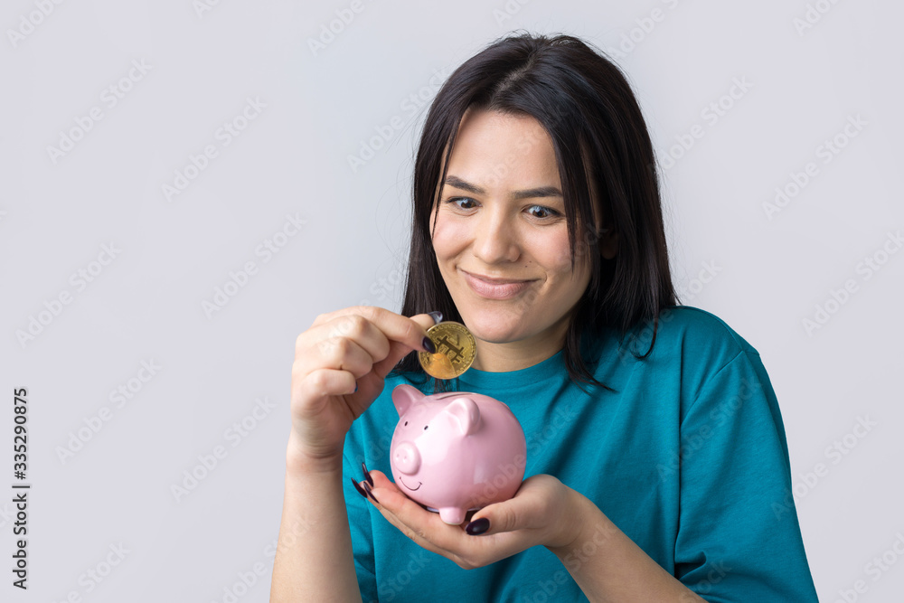 The girl holds a pink piggy bank and a coin in her hands. The concept of wealth and accumulation. The girl holds a pink piggy bank and a coin in her hands. The concept of wealth and accumulation.