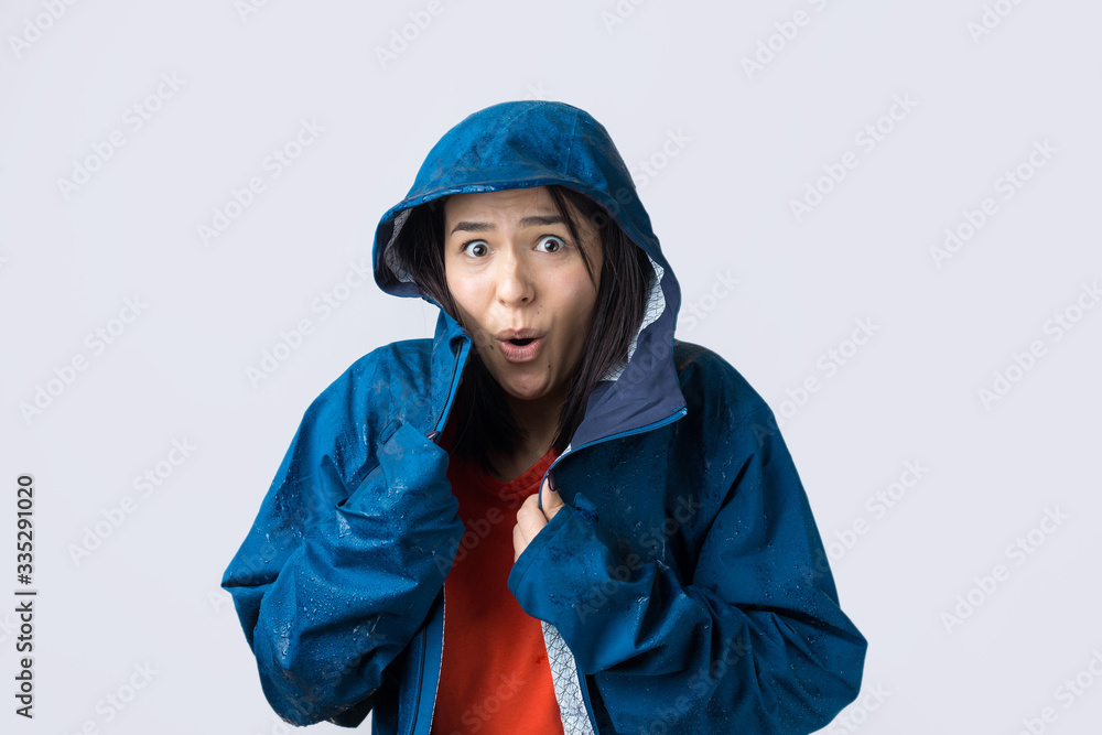 Portrait of a smiling girl dressed in blue raincoat in drops posing with hood on grey background in a studio. Portrait of a smiling girl dressed in blue raincoat in drops posing with hood on grey background in a studio.