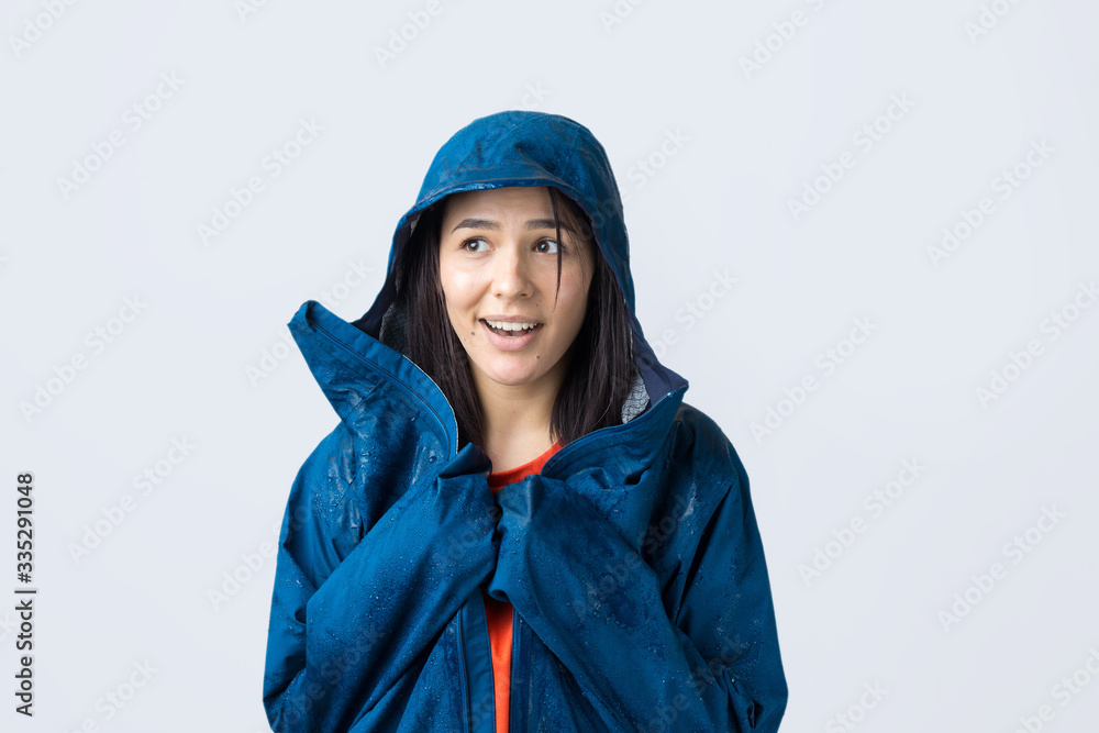 Portrait of a smiling girl dressed in blue raincoat in drops posing with hood on grey background in a studio. Portrait of a smiling girl dressed in blue raincoat in drops posing with hood on grey background in a studio.