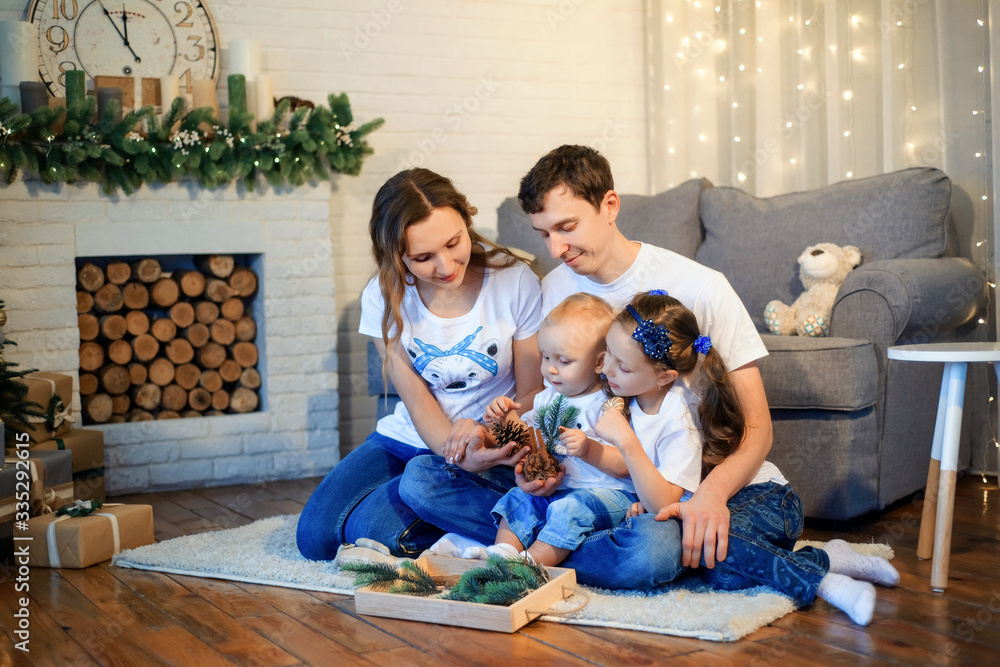 Theme Christmas and New Year family circle. Young Caucasian family with 1 year old son and 6 years old daughter sitting on floor in living room. Christmas decorations. Boy and girl kids and parents Theme Christmas and New Year family circle. Young Caucasian family with 1 year old son and 6 years old daughter sitting on floor in living room. Christmas decorations. Boy and girl kids and parents