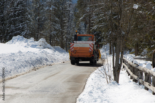 Orange-coloured Snowplough Operating on the Road with Snow on the Edges