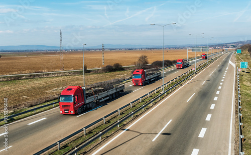 Convoy of Red Utility Transportation Trucks carrying load of Steel Wires for Construction on a rural countryside highway under a beautiful blue sky