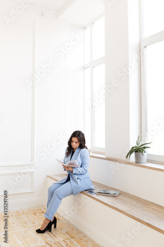 Portrait of an attractive working girl freelancer businesswoman with black hair in a stylish blue suit against a white textured wall in the office at home