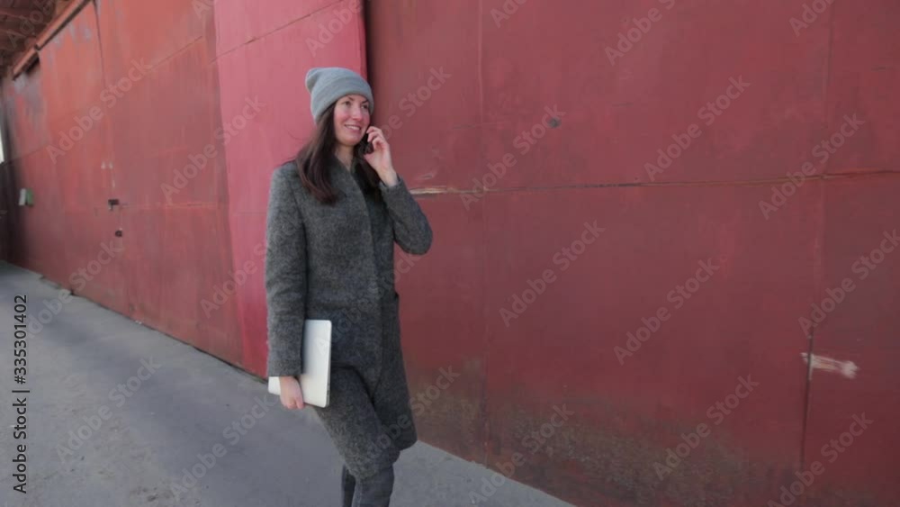 Business woman walking on the city street with a modern laptop wearing trendy clothes in sunny day and talking on the phone Business woman walking on the city street with a modern laptop wearing trendy clothes in sunny day and talking on the phone