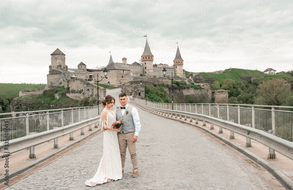 Obraz premium Stylish bride and groom. Just merried. wedding couple.Close up. Happy bride and groom on their wedding day. Groom and Bride walking near old castle. wedding dress. Bridal wedding bouquet of flower
