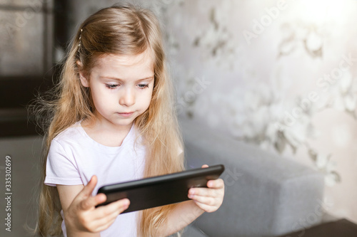A little girl with long blond hair is home-schooled. A child with a tablet computer watches lessons online. home schooling