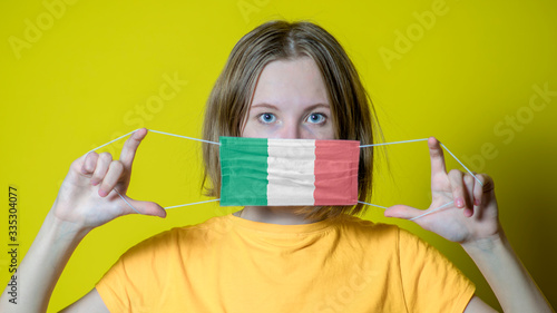 Teen girl anearing hygienic face mask painting Italian flag to protect from the Coronavirus 2019 (COVID-19) photo