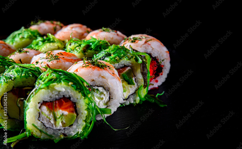set of Sushi rolls with seafood, srimp, cream cheese,caviar and Chuka salad on black wooden table background set of Sushi rolls with seafood, srimp, cream cheese,caviar and Chuka salad on black wooden table background