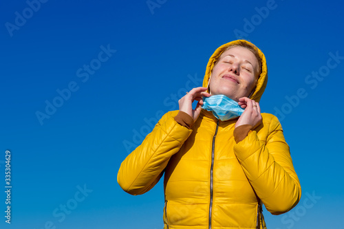 Close up portrait of a satisfied girl taking off his medical mask and inhaling fresh clean air on an open-air street during a coronovirus quarantine pandemic.