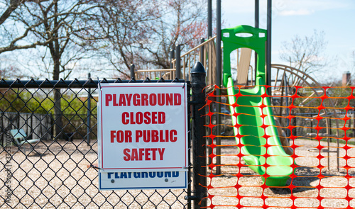 Playground closed for public safety sign posted with orange netting closing the opening of play area photo