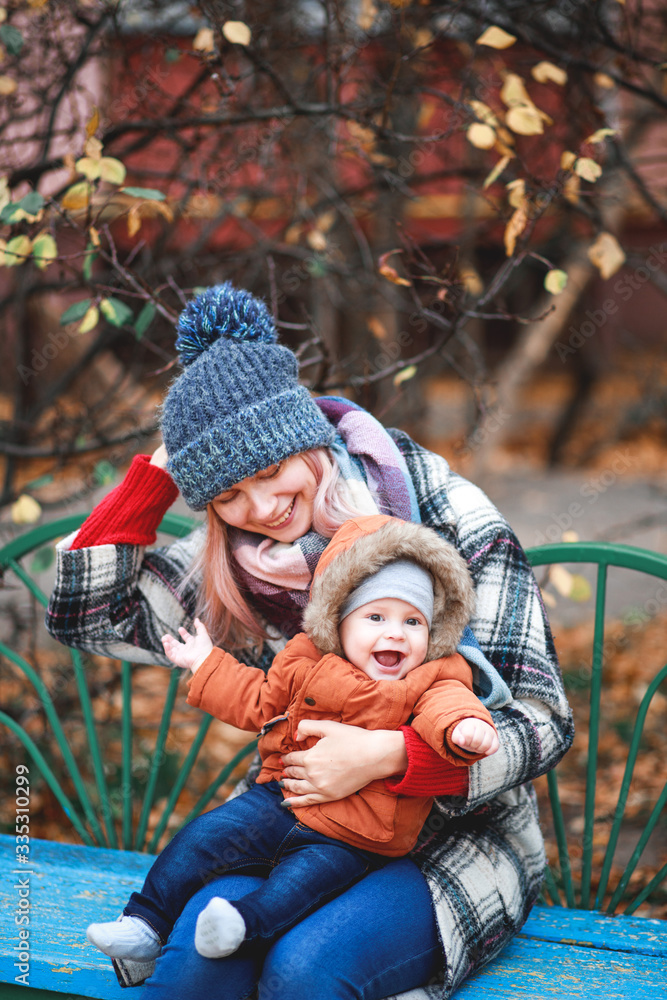 Obraz premium A stylish young mother with a small son in her arms walks in the autumn.