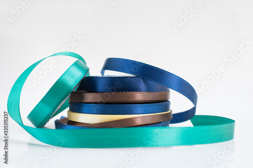 Stack of satin ribbon coils. Blue, green, brown and yellow ribbon for handmade. Needlework items.