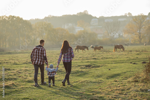 Family with cute little son. Father in a red shirt. People walking near horses.