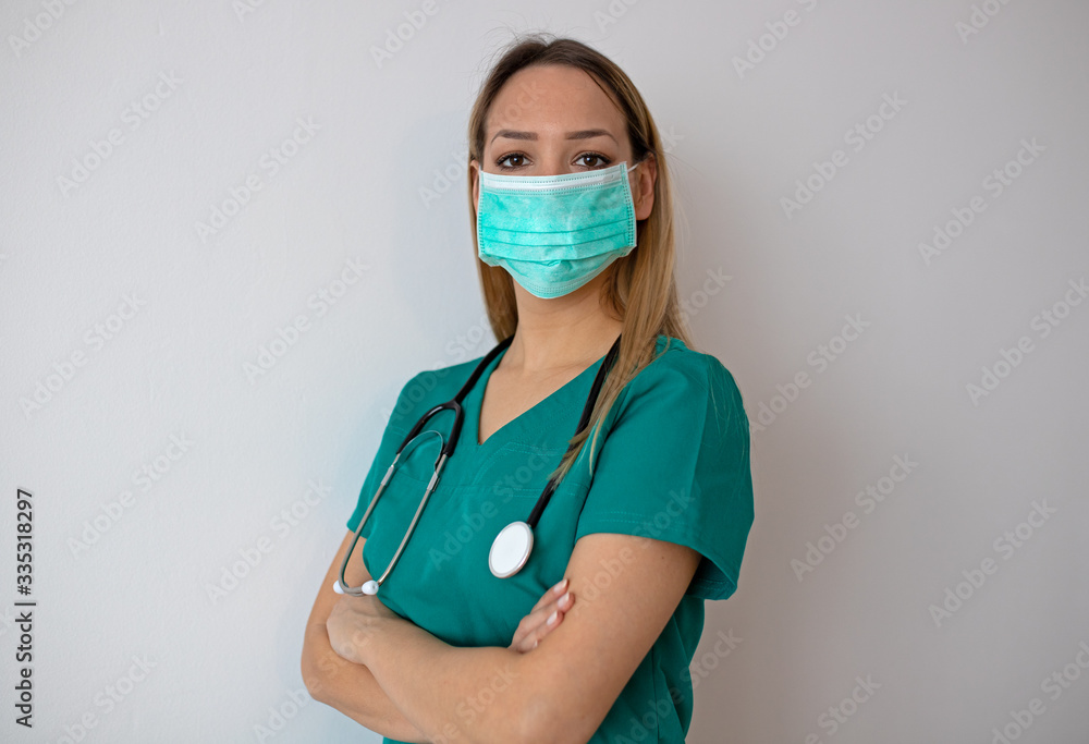 Female nurse standing arms crossed. Confident young woman doctor. Female nurse young pretty woman in green clothes with medical mask posing. Female nurse standing arms crossed. Confident young woman doctor. Female nurse young pretty woman in green clothes with medical mask posing.