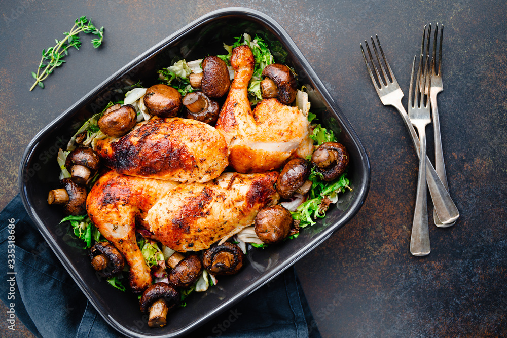 Top view of roasted chicken legs and breasts with fresh salad and mushrooms in black dish. Top view of roasted chicken legs and breasts with fresh salad and mushrooms in black dish.