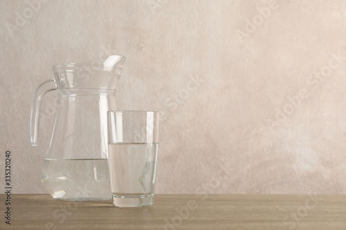 Jug with water and glass on wooden table, space for text