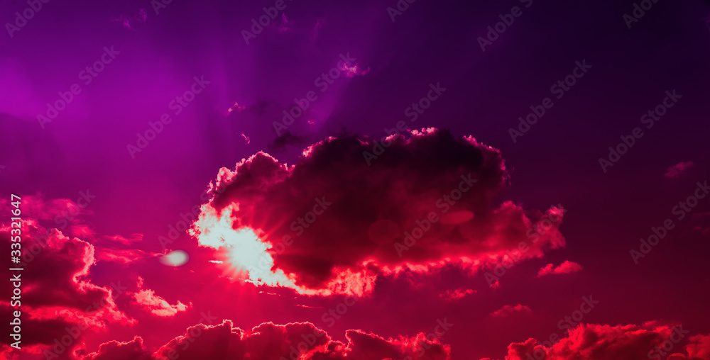 The bright sun shines through the red clouds. Apocalypse in the sky, red sky and gloomy dark clouds. The rays of the sun break through the clouds. Designer background.