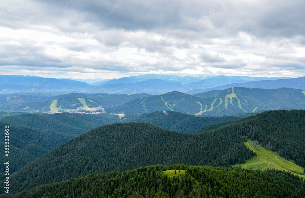 Tracks of famous Bukovel ski resort in summer, Carpathian mountains, Ukraine. Green forests, hills, grassy meadows and cloudy sky