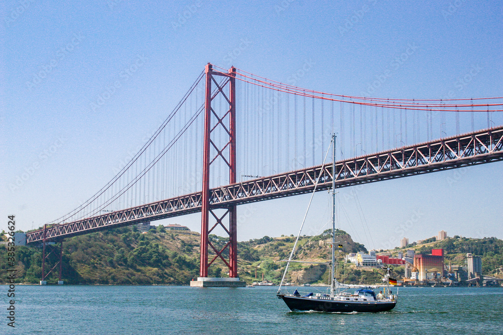 sailing yacht passing the Bridge of the 25 th of April, over the river Tejo in Lisbon, Portugal sailing yacht passing the Bridge of the 25 th of April, over the river Tejo in Lisbon, Portugal