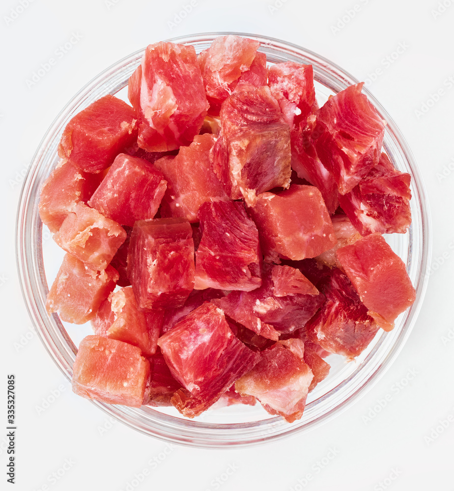 Iberian ham (serrano) cut into cubes (diced). In glass bowl. Isolated on white background. Iberian ham (serrano) cut into cubes (diced). In glass bowl. Isolated on white background.