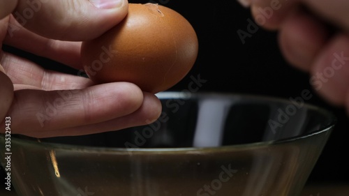 Hands holding one brown organic egg. Cracking over glass bowl. Close up.