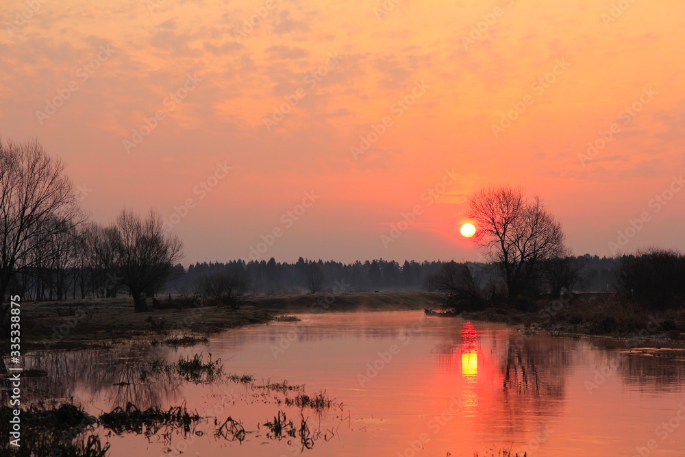 Bright orange sunrise over the river in March