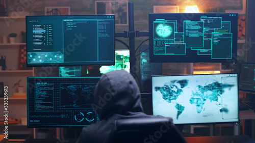 Back view of hooded cyber terrorist using super computer