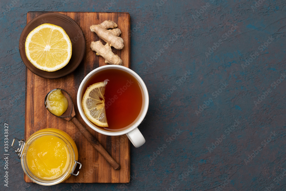 flat lay of natural ingredients for tea to increase immuntiy during self-isolation period. lemon on a wooden plate, ginger, hot tea and honey in a wooden spoon. flat lay of natural ingredients for tea to increase immuntiy during self-isolation period. lemon on a wooden plate, ginger, hot tea and honey in a wooden spoon.