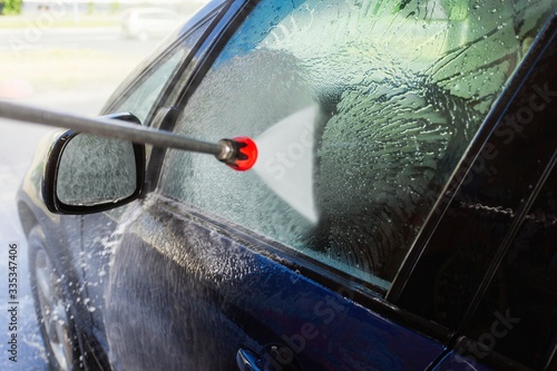 Close-up of man holding a high-pressure water sprayer for door car washing. Contactless self-service car wash. Concept disinfection and antiseptic cleaning of the vehicle, corvid-19 and coronavirus