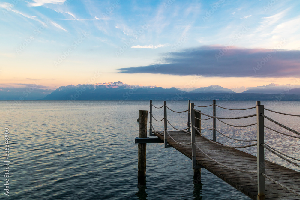 Naklejka premium Coucher de soleil sur le Lac Léman et les montagnes des Alpes à Morges avec au premier plan un ponton (Suisse)