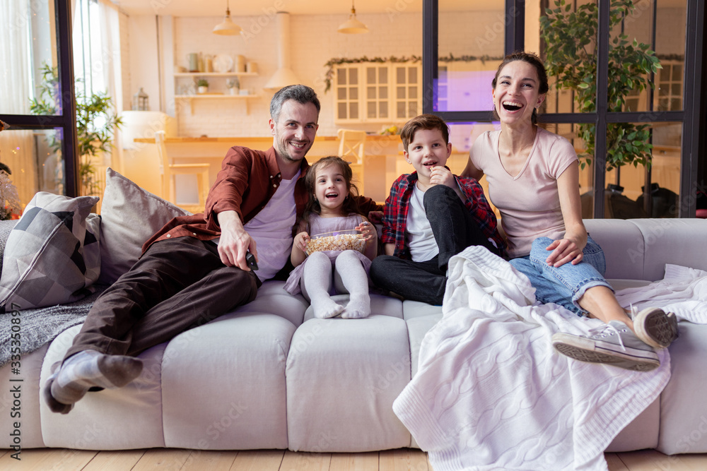 Parent and children watching funny tv-show program on television eating popcorn snack and laughing loudly. Parent and children watching funny tv-show program on television eating popcorn snack and laughing loudly.