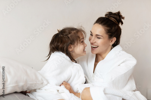 Mother and daughter having fun after bath or shower sitting in bed. 