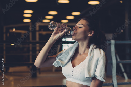 Gorgeous young woman with a towel on her shoulders drinking water from a bottle at the gym
