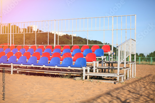 Empty Volleyball court at the city beach. Nobody is on the summer beach due to quarantine infection. Outdoor sports competition. Close up view of plastic chairs on the stadium bench.