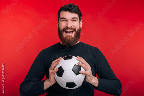 Photo of cheerful young man holding soccer ball and screaming over red background © Vulp