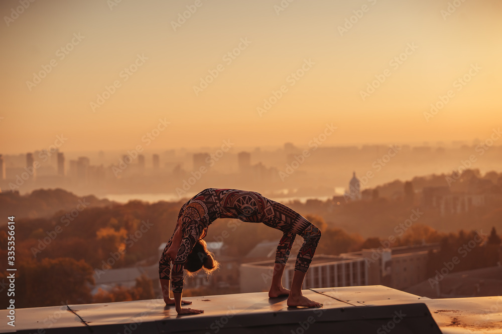 Fototapeta premium Woman doing yoga on the roof of a skyscraper in big city.