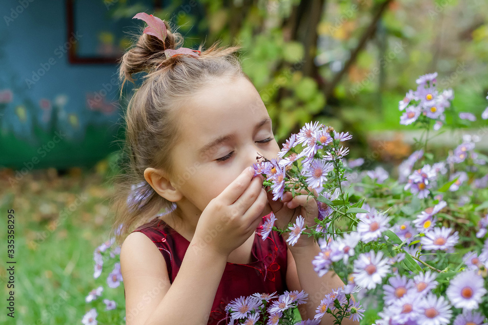 a beautiful girl in a red dress sniffs purple flowers. in the middle of a blooming garden. a beautiful girl in a red dress sniffs purple flowers. in the middle of a blooming garden.