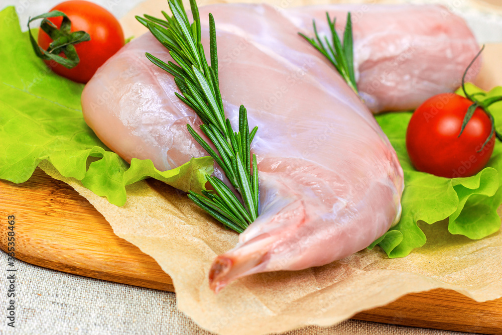 Raw uncooked pink rabbit leg meat with green rosemary and fresh vegetables on light wooden cutting board background. Raw uncooked pink rabbit leg meat with green rosemary and fresh vegetables on light wooden cutting board background.